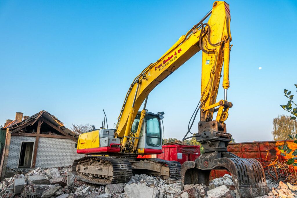 A large yellow excavator working amidst rubble at a construction site under a clear blue sky.